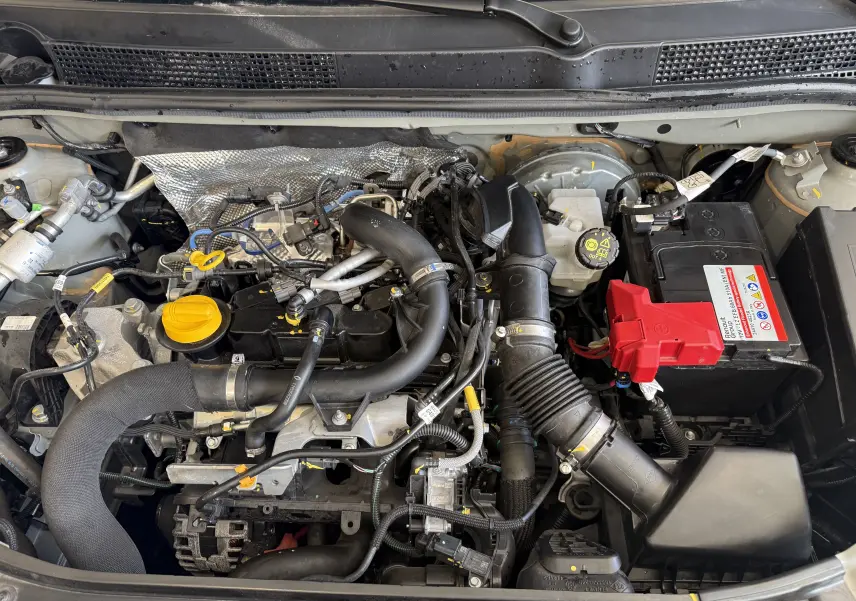 Vue plongeante sur le moteur essence gris d'une Dacia Sandero 1.0 TCe 90ch Journey avec batterie et durites visibles.