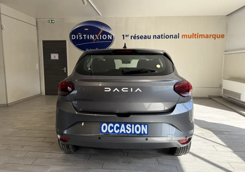Vue arrière d'une Dacia Sandero gris métallisé 2025 en showroom avec plaque "OCCASION" visible.