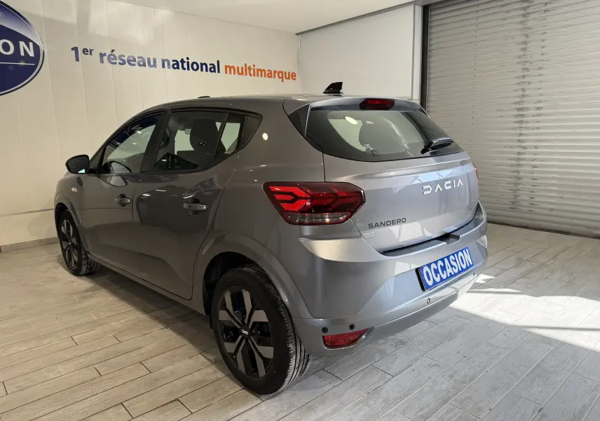 Vue 3/4 arrière droite d'une Dacia Sandero gris métallisé 2025 avec feux LED et jantes noires distinctives.