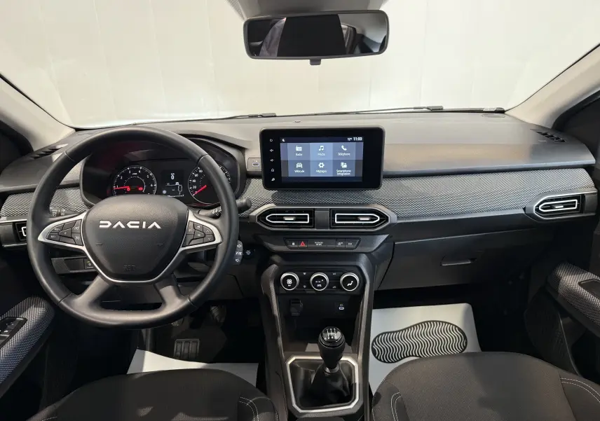 Vue intérieure frontale du tableau de bord gris et noir du Dacia Sandero 2025 avec écran tactile et boîte manuelle.