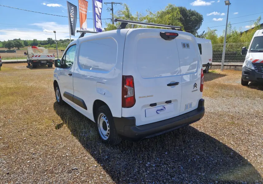 Vue 3/4 arrière droite d'un Citroën Berlingo blanc utilitaire avec porte latérale pleine et barres de toit noires.