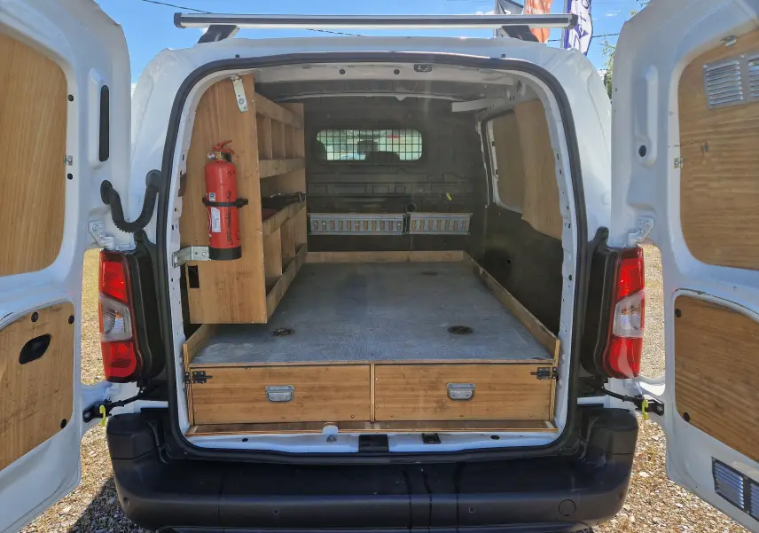 Vue arrière ouverte du Citroën Berlingo blanc 2020, montrant l'aménagement bois intérieur avec étagères et extincteur.