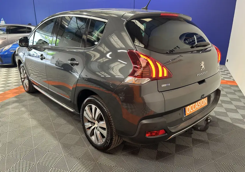 Peugeot 3008 gris en 3/4 arrière droit, avec feux arrière allumés et attelage visible sous le pare-chocs.