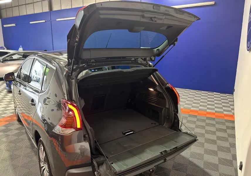 Vue arrière gauche d’un Peugeot 3008 gris avec coffre ouvert et hayon relevé, montrant l’espace de chargement intérieur.