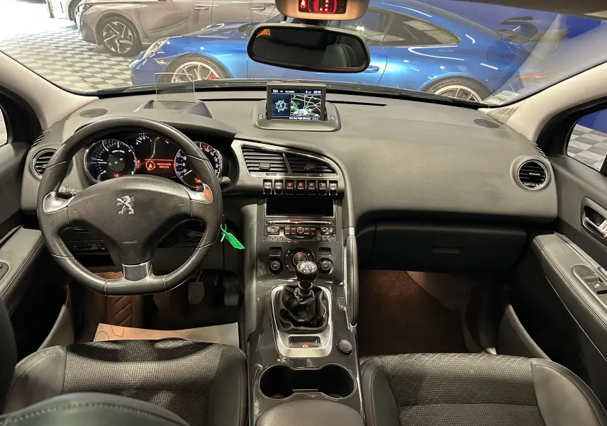 Vue intérieure frontale du Peugeot 3008 gris de 2015, montrant le tableau de bord, volant, boîte manuelle et écran central GPS.