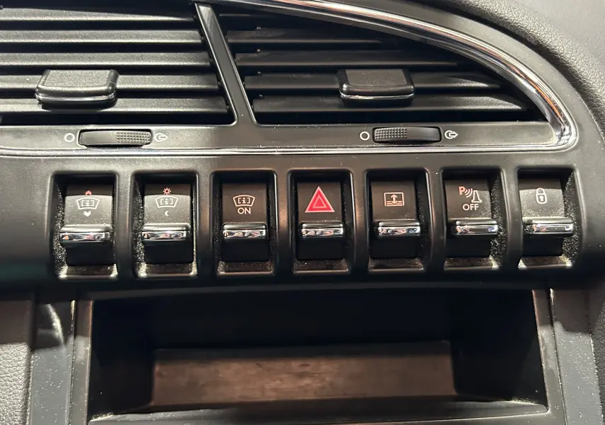 Gros plan sur les commandes noires du tableau de bord du Peugeot 3008, avec boutons d'alerte et fonctions variées.