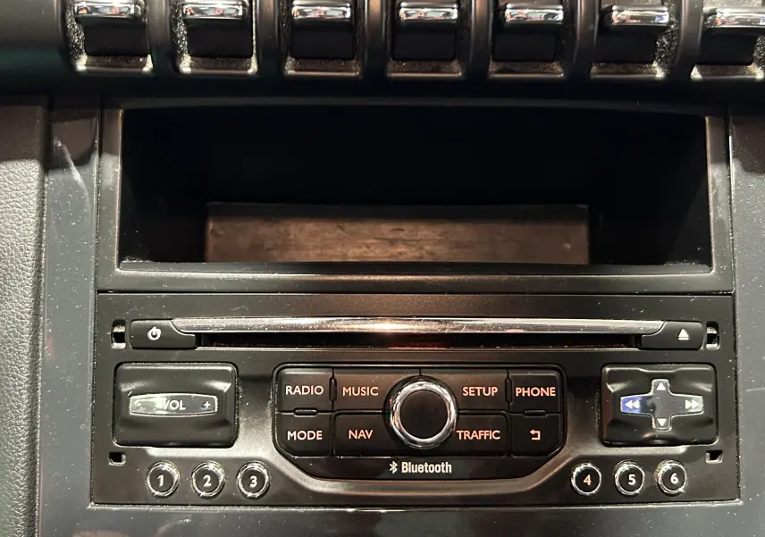 Gros plan sur la console centrale noire du Peugeot 3008 gris, avec commandes radio, navigation et Bluetooth visibles.