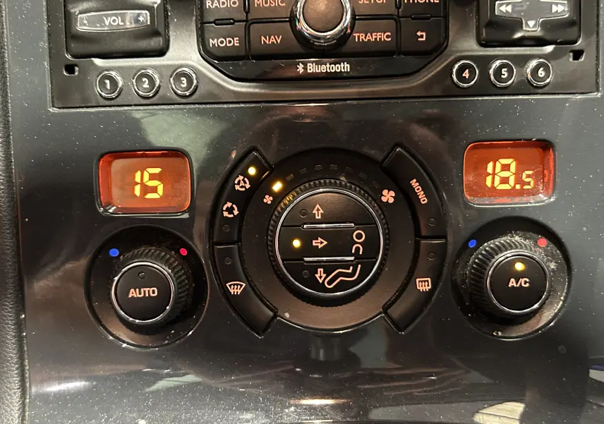 Gros plan sur la console centrale du Peugeot 3008 gris, montrant les commandes de climatisation et radio avec affichage digital orange.