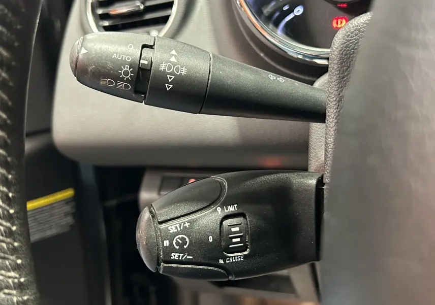 Gros plan sur les commandes de phares et régulateur de vitesse du Peugeot 3008 gris, côté gauche du volant.