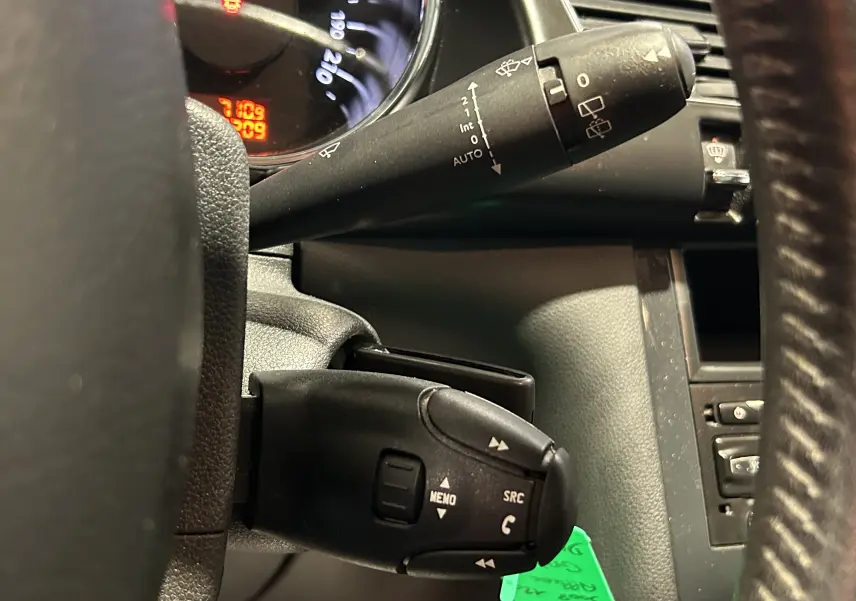 Gros plan sur les commandes au volant côté gauche du Peugeot 3008 gris, montrant les boutons de gestion audio et essuie-glace.