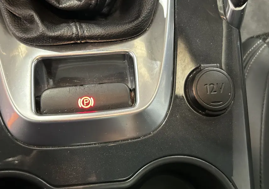 Gros plan sur la console centrale du Peugeot 3008 gris, montrant le frein à main électronique et la prise 12V.