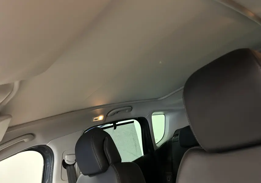 Vue intérieure arrière gauche du Peugeot 3008 gris, montrant les sièges en cuir et le toit panoramique avec store partiellement déployé.
