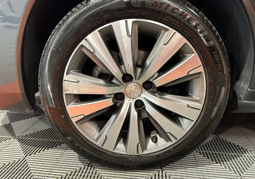 Gros plan sur la roue avant droite du Peugeot 3008 gris, mettant en valeur la jante alliage et le pneu Michelin.