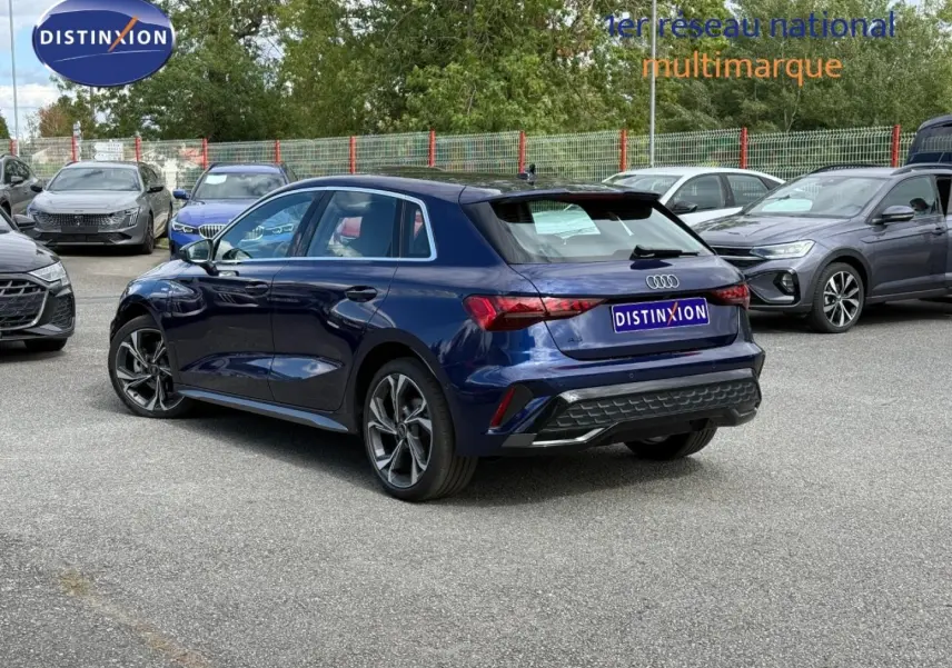 Audi A3 Sportback bleu Navarre métallisé vue 3/4 arrière droit sur parking avec jantes alu distinctives.