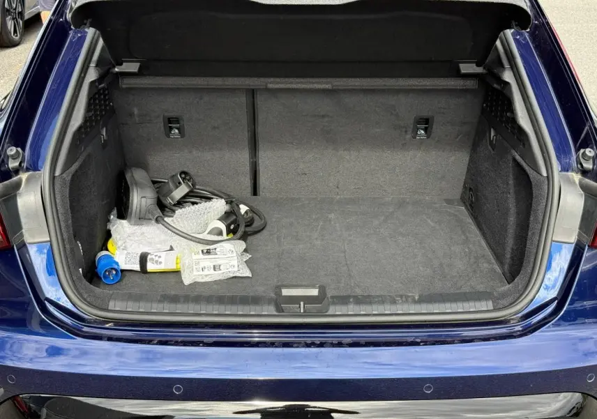 Coffre ouvert vu de l'arrière d'une Audi A3 Sportback 2025 bleu Navarre métallisé avec câbles de recharge visibles.