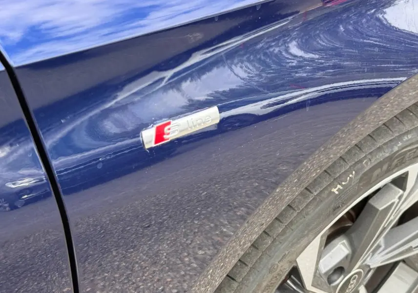 Gros plan sur l’aile avant droite bleu Navarre métallisé avec logo S line et jante alu Audi A3 Sportback 2025.