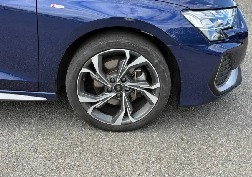 Gros plan sur la roue avant droite et partie avant bleue métallisée d'une Audi A3 Sportback S line 2025.