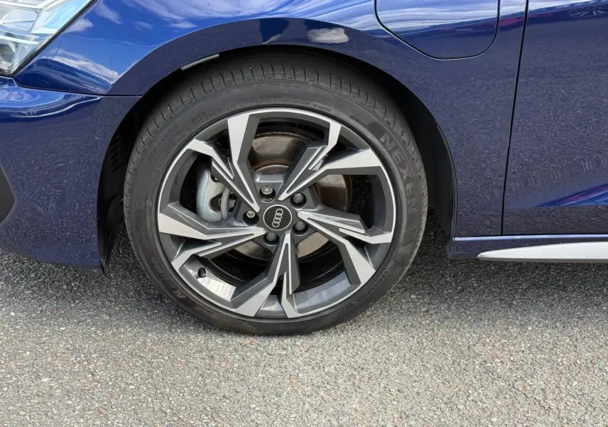 Gros plan sur la roue avant gauche d’Audi A3 Sportback Bleu Navarre métallisé avec jante alliage S line et logo Audi.