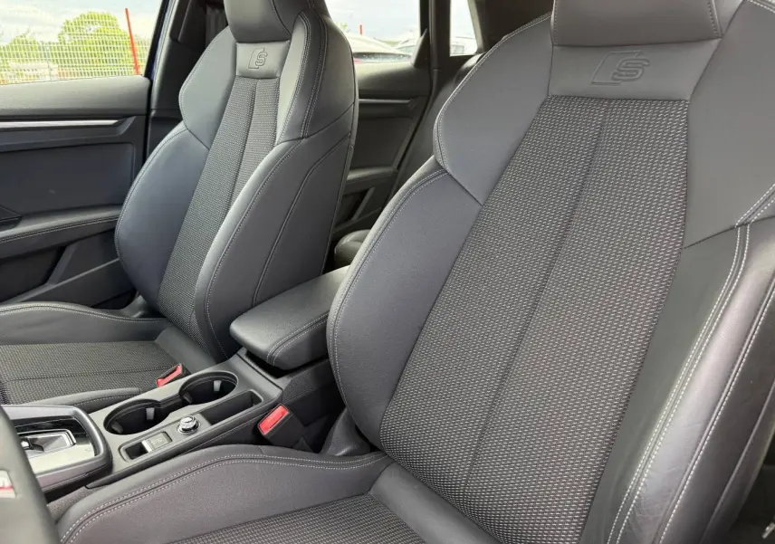 Gros plan sur les sièges avant sport noirs avec logo S embossé, accoudoir central et console d'une Audi A3 Sportback 2025.