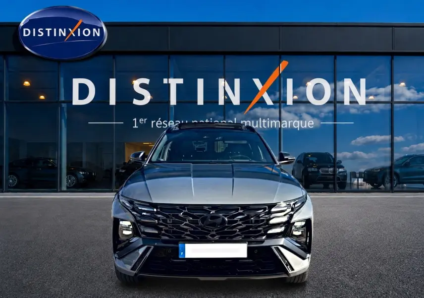 Vue frontale d'un Hyundai Tucson gris shadow 2026 avec calandre noire et phares LED devant un showroom Distinxion.