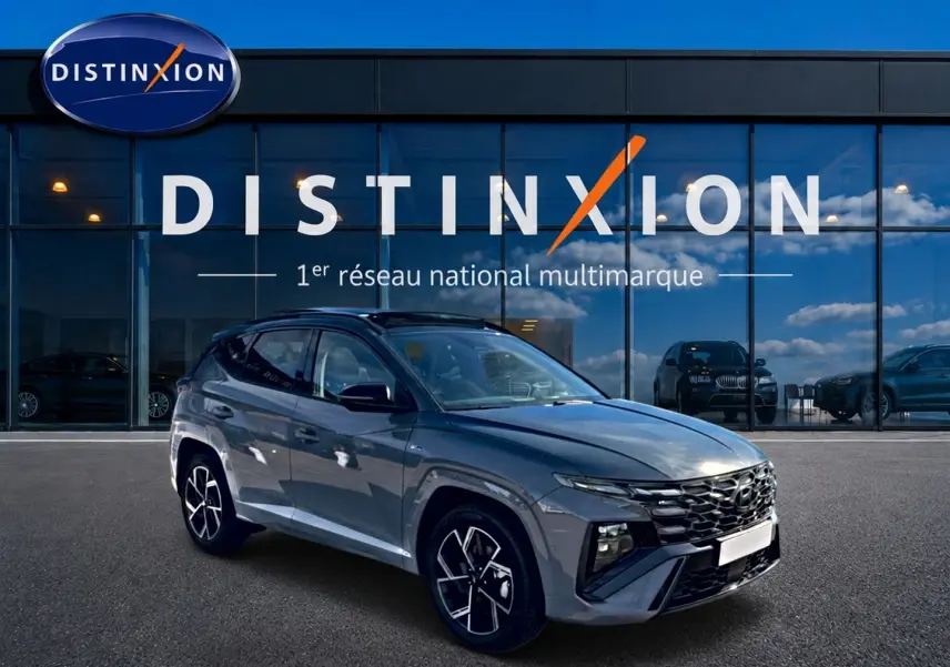 Hyundai Tucson gris shadow en 3/4 avant droit, avec calandre noire et jantes alu distinctives, devant vitrine Distinxion.