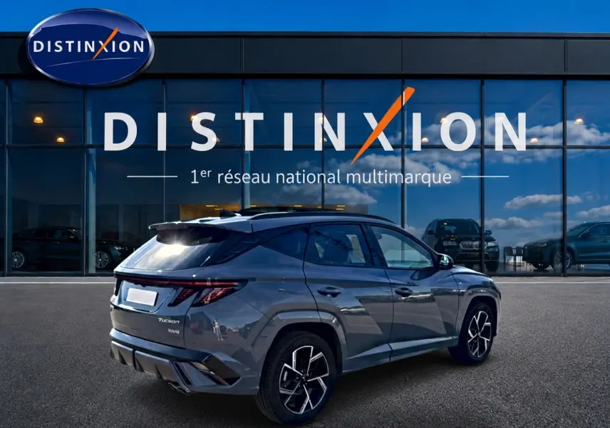 Vue 3/4 arrière droite d’un Hyundai Tucson gris shadow avec jantes alu et feux arrière LED, devant un showroom Distinxion.