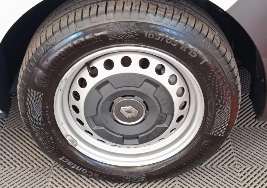 Gros plan sur la roue avant droite avec jante acier et logo Renault, partie blanche de la carrosserie visible.