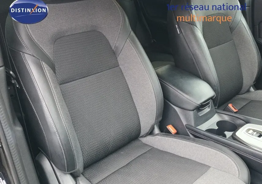 Gros plan sur les sièges avant en tissu et cuir noir du Nissan Qashqai e-POWER 2025, avec accoudoir central visible.