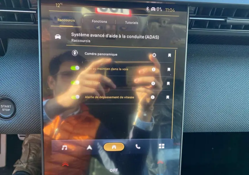Écran tactile central du Citroën C5 Aircross 2026 affichant les aides à la conduite, avec reflet d'une personne en gilet orange.