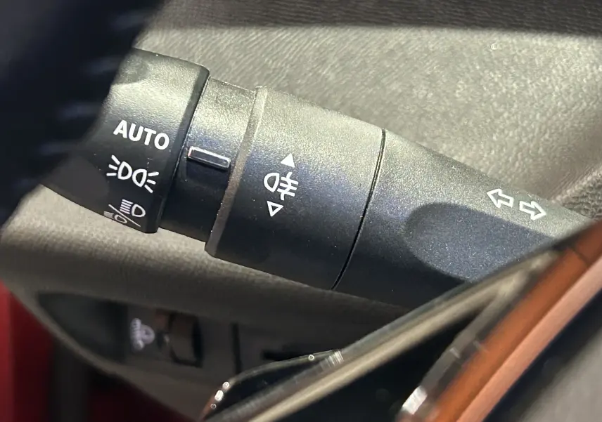 Gros plan sur la commande des phares automatiques et clignotants dans l’habitacle d’une Peugeot 308 rouge 2024.