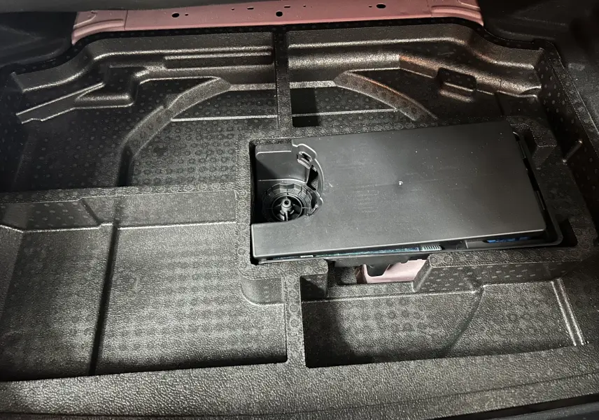 Vue rapprochée du compartiment de rangement sous le coffre d'une Peugeot 308 rouge, avec espace pour outils.