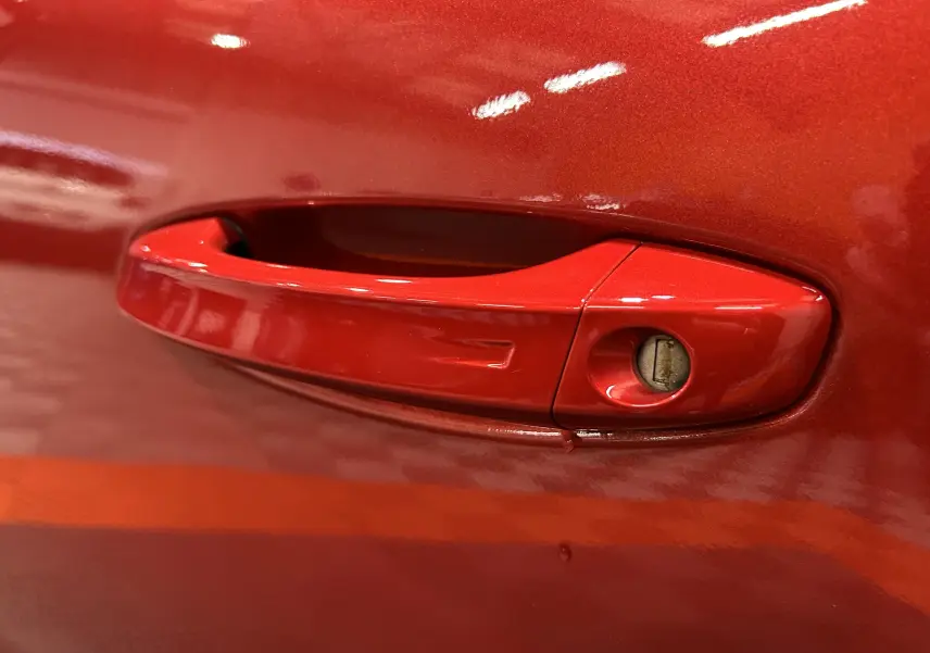 Poignée de porte rouge de la Peugeot 308 BlueHDi 130 Allure 2024, vue en gros plan sur la serrure intégrée.