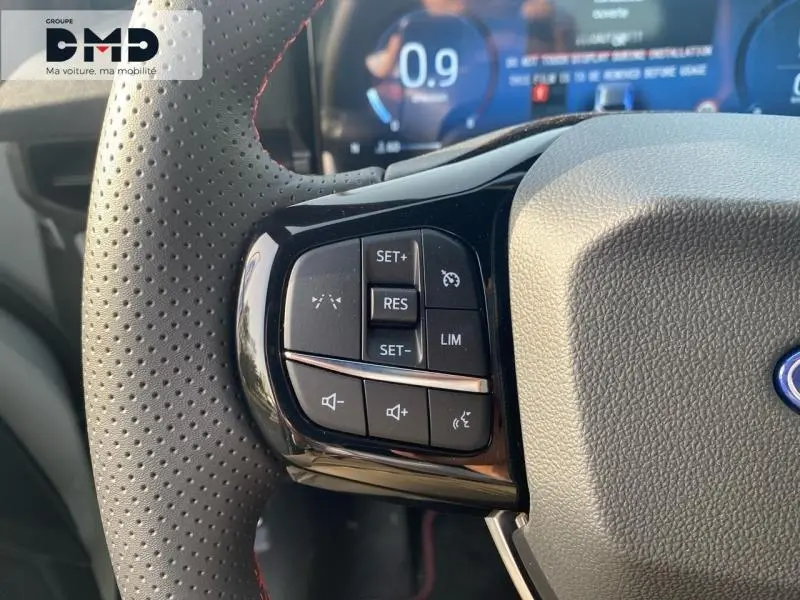 Gros plan sur les commandes du volant perforé gris du Ford Puma 2026, avec affichage numérique en arrière-plan.