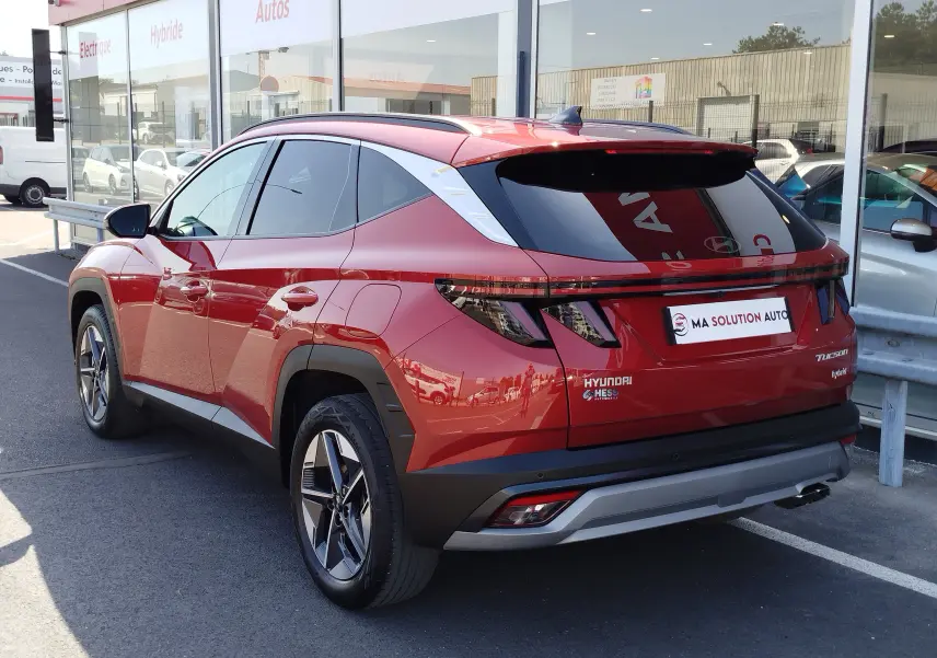 Vue 3/4 arrière droite du Hyundai Tucson 2024 hybride en rouge Ultimate Red Métal avec feux arrière LED et jantes bi-ton.