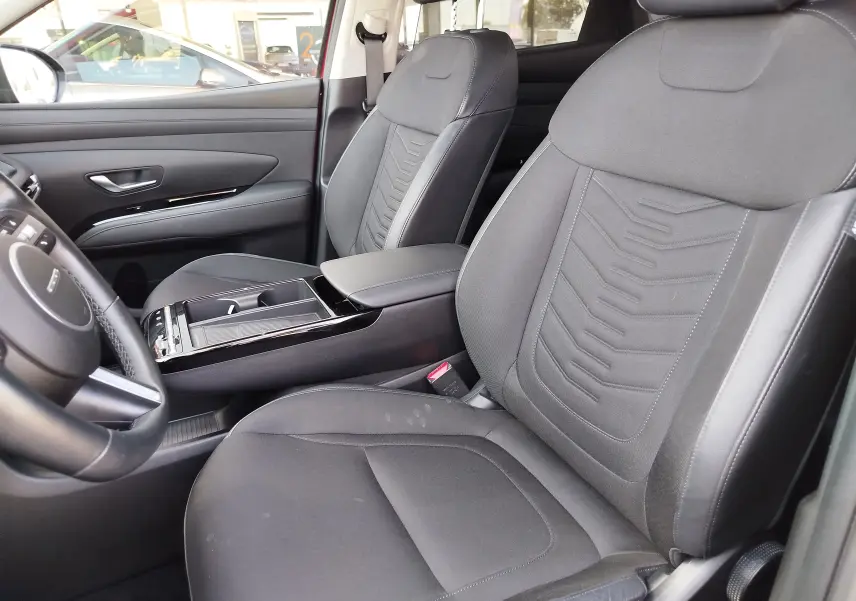 Vue intérieure du Hyundai Tucson 2024, sièges avant en tissu gris foncé avec console centrale et volant partiel visible.