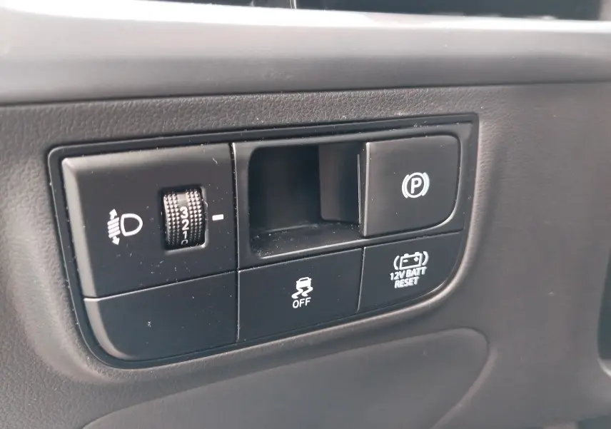 Gros plan sur les commandes intérieures noires du Hyundai Tucson 2024, avec réglage phares et frein de parking électrique.