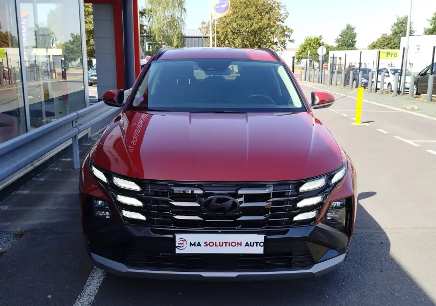 Vue frontale d'un Hyundai Tucson 2024 rouge Ultimate Red Métal avec calandre noire et feux LED distinctifs allumés.