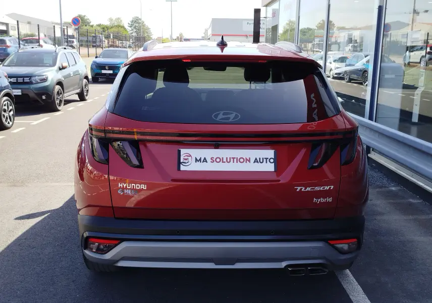 Vue arrière d'un Hyundai Tucson 2024 hybride en rouge Ultimate Métal, avec feux arrière LED et double sortie d'échappement.