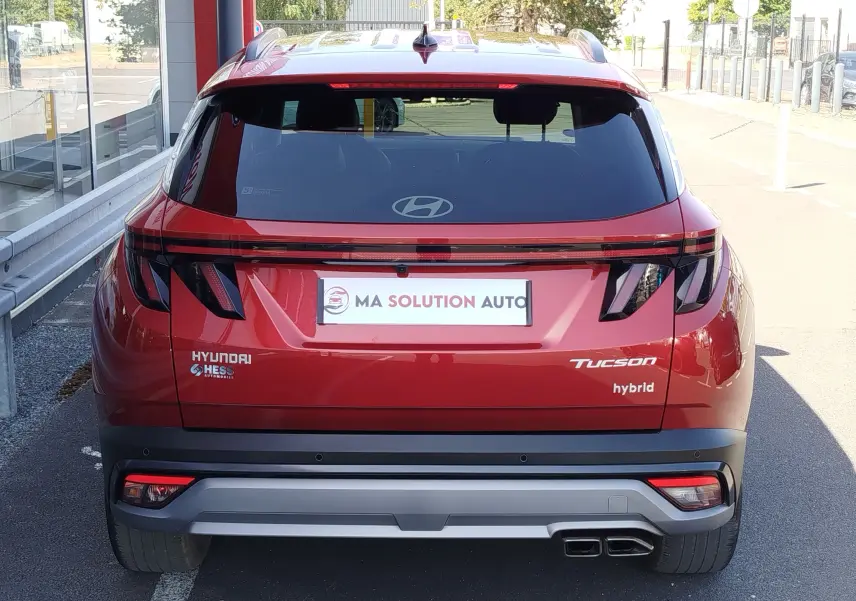 Vue arrière d'un Hyundai Tucson hybride 2024 en rouge Ultimate Red Métal avec feux arrière LED et double sortie d'échappement.