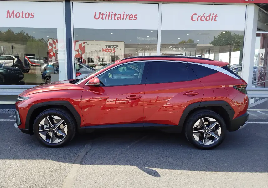 Vue de profil côté gauche du Hyundai Tucson 2024 hybride en rouge Ultimate Red Métal avec jantes bi-ton et détails noirs.