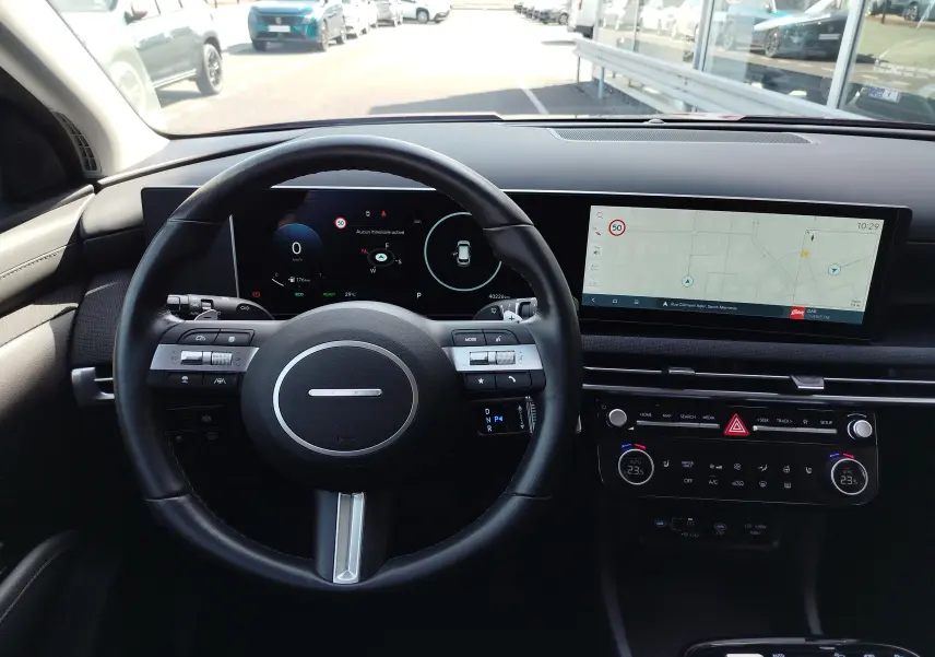 Vue intérieure du tableau de bord du Hyundai Tucson 2024, avec volant noir et double écran numérique affichant navigation et informations.