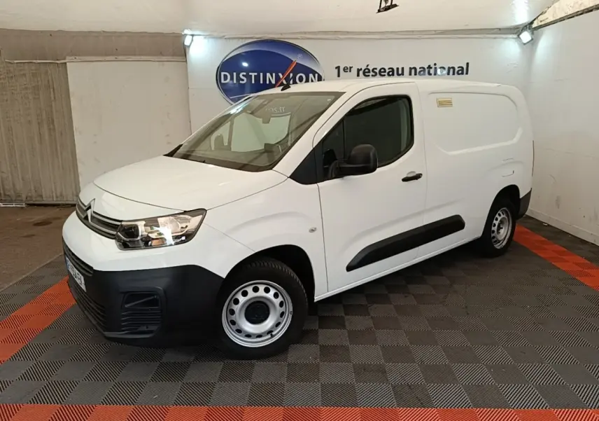 Vue 3/4 avant droite d’un utilitaire Citroën Berlingo XL blanc avec pare-chocs noirs et jantes acier en intérieur showroom.