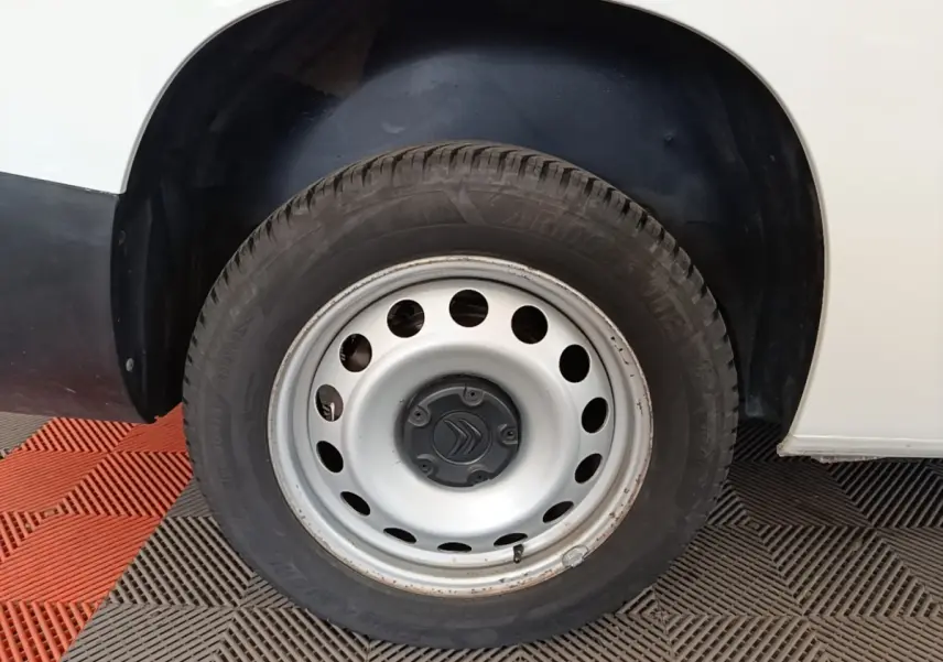 Gros plan sur la roue avant gauche d’un Citroën Berlingo blanc avec jante acier et logo Citroën central.