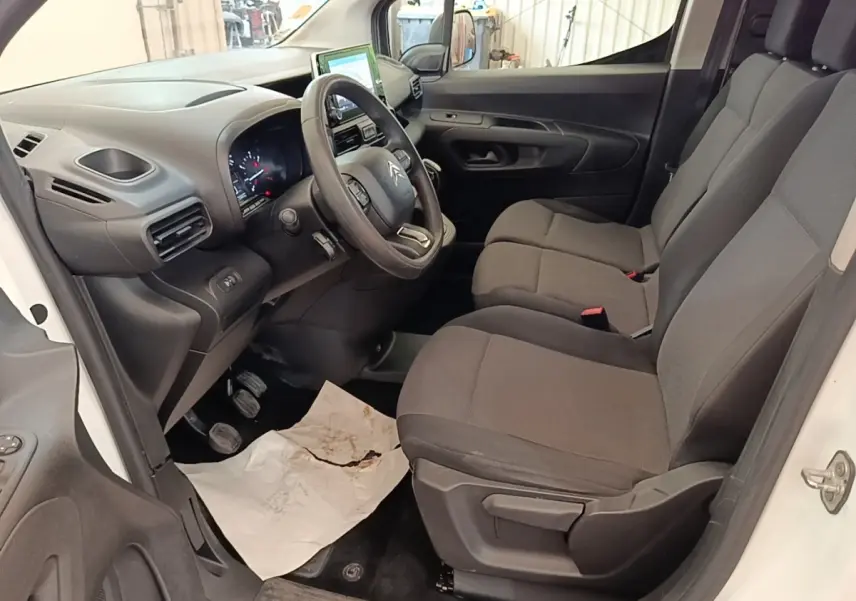 Intérieur côté conducteur du Citroën Berlingo blanc, montrant le volant multifonctions et les sièges tissu gris.