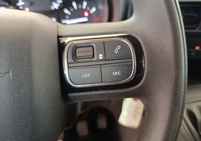 Gros plan sur les commandes noires multifonctions à gauche du volant du Citroën Berlingo 2020, intérieur sombre.
