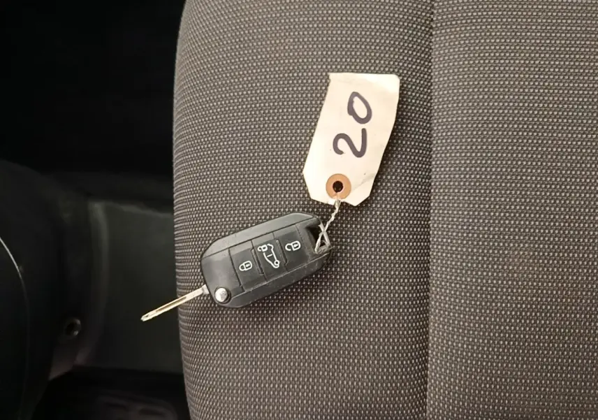 Clé de voiture noire avec étiquette "20" posée sur un siège tissu gris foncé à l'intérieur d'un Citroën Berlingo blanc.