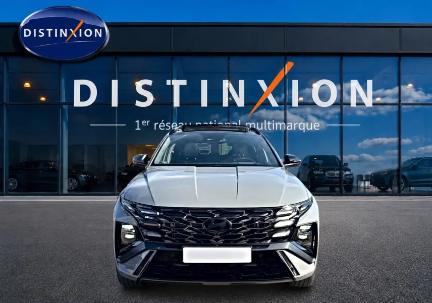 Vue avant du Hyundai Tucson 2026 gris shadow avec calandre noire et phares LED, devant une vitrine Distinxion.