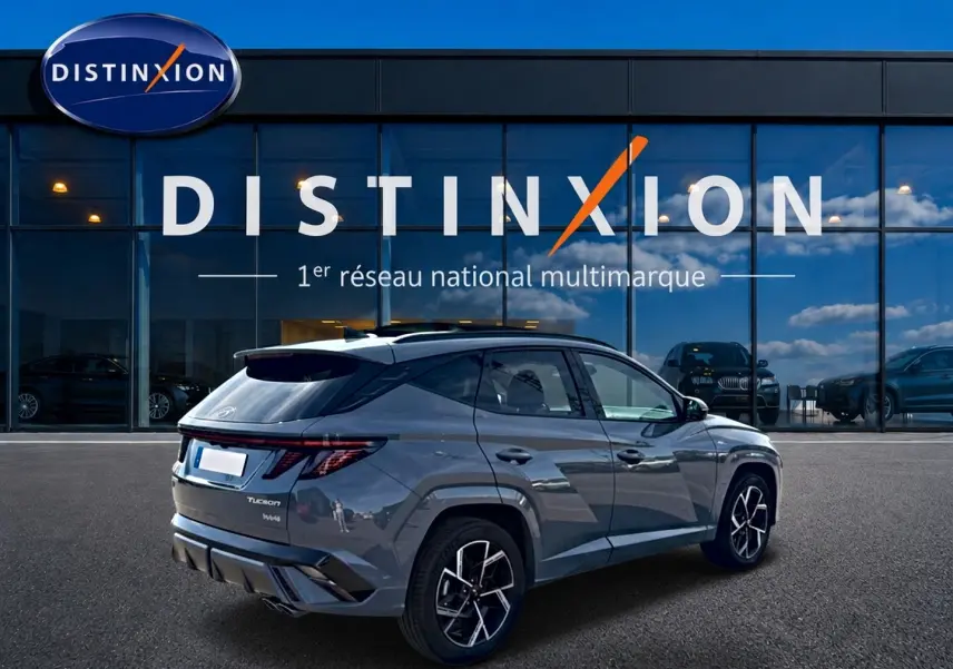 Vue 3/4 arrière droite d'un Hyundai Tucson gris shadow avec jantes alu et feux arrière LED, devant un showroom Distinxion.