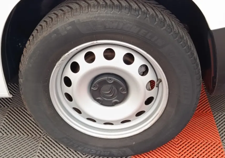 Gros plan sur la roue avant droite d’un Citroën Berlingo blanc avec jante acier et pneu Michelin.