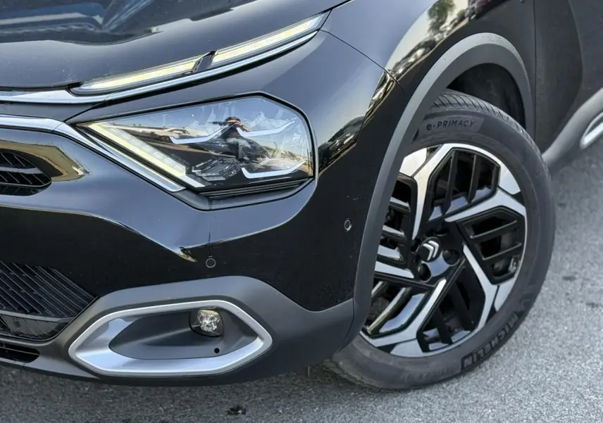 Gros plan sur l'avant droit noir Perla du Citroën C4 X 2024, mettant en valeur le phare LED et la jante alliage 18'' Aeroblade.